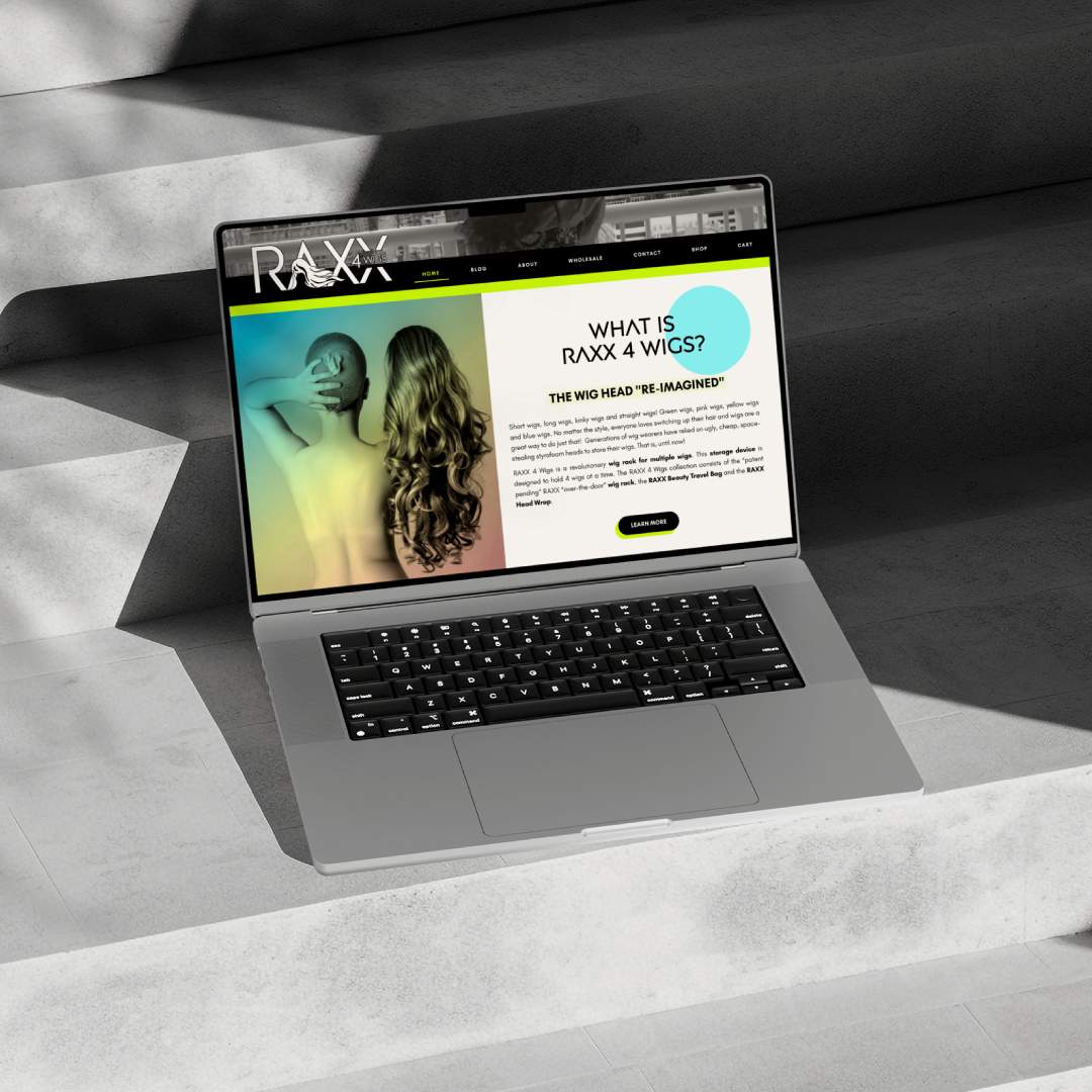 Macbook mockup of Raxx 4 Wigs website homepage against a concrete background.